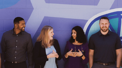 A diverse group of people interacting by a purple wall.