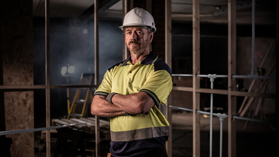 A man in a hard hat standing in front of plumbing work in a new build.