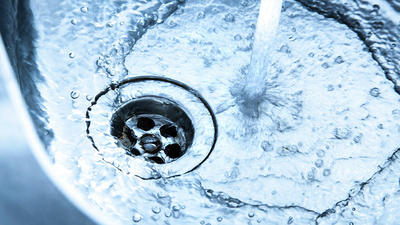 Close up of a Stainless steel kitchen sink with running water. The faucet is turned right up. a strong water jet flows into the basin. small bubbles and swirls are seen. the water flows through the open drain. sharp and detailed image. blue toned.