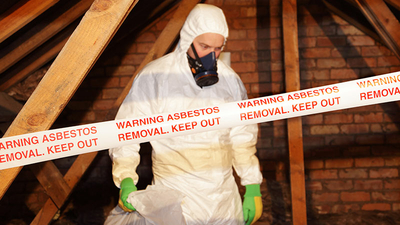 A worker wearing protective clothing while clearing the hazardous substance, asbestos, from an old attic.
