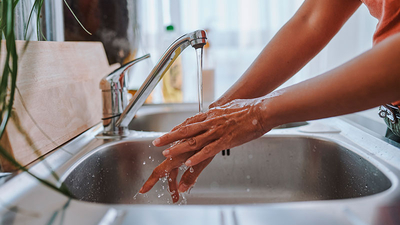 Woman practices personal hygiene, washing hands thoroughly under running water in kitchen sink